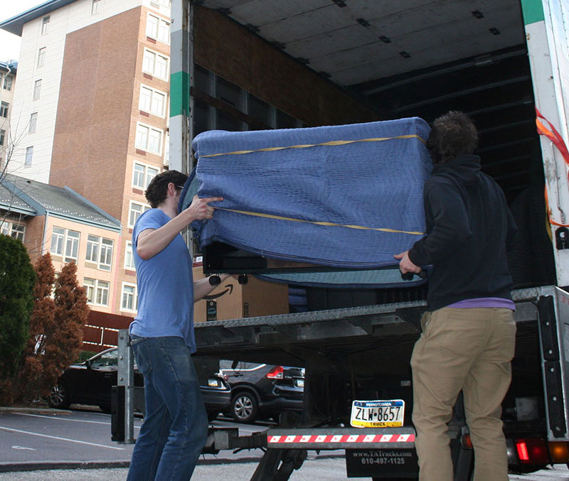 Two movers from Broad Street Movers taking extra care while loading furniture wrapped in furniture blankets into the moving truck